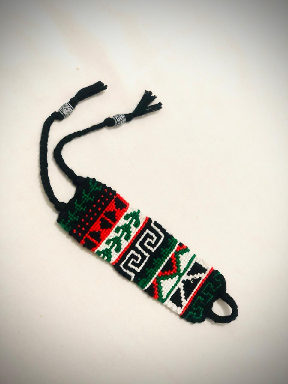 Handmade macramé bracelet with red, black, green, and white tribal-inspired geometric patterns, braided ties, and silver accent beads.