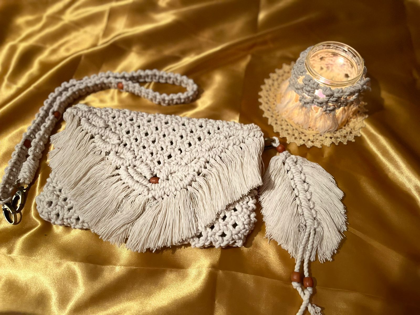Handmade macramé shoulder bag with fringe flap, wooden bead accents, and matching woven strap displayed on golden fabric.